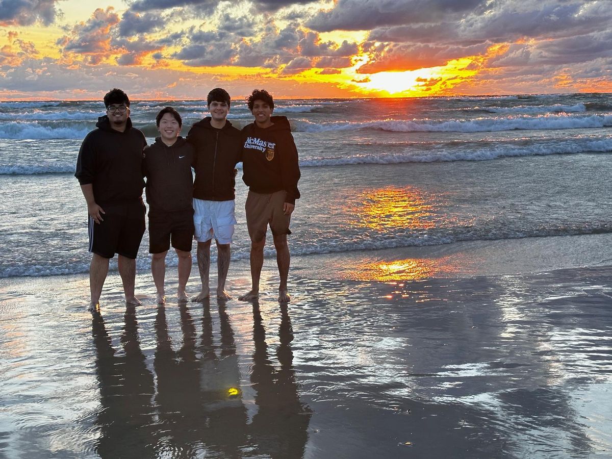 Four of us standing on a wet beach at sunset, the sky orange over the water.