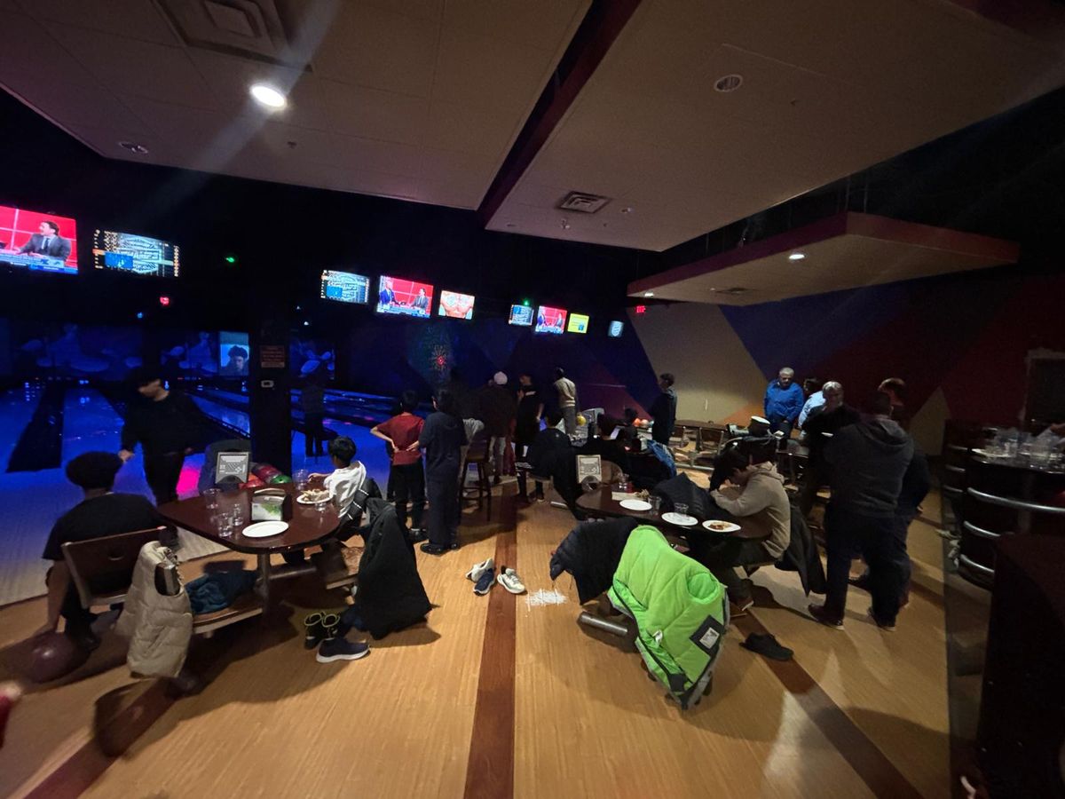 A busy bowling alley, lanes and screens lit up in the dark.