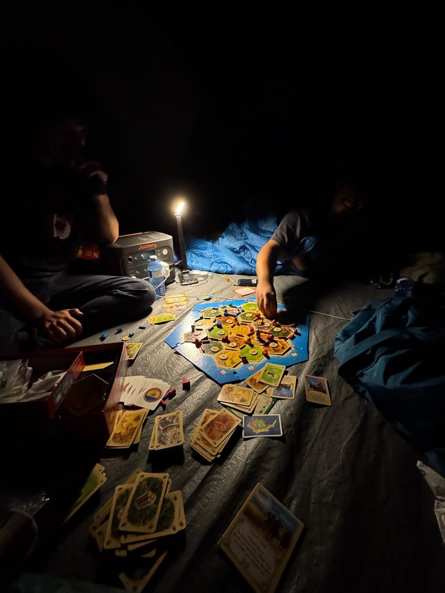A card game spread out on a groundsheet by lantern light at night.