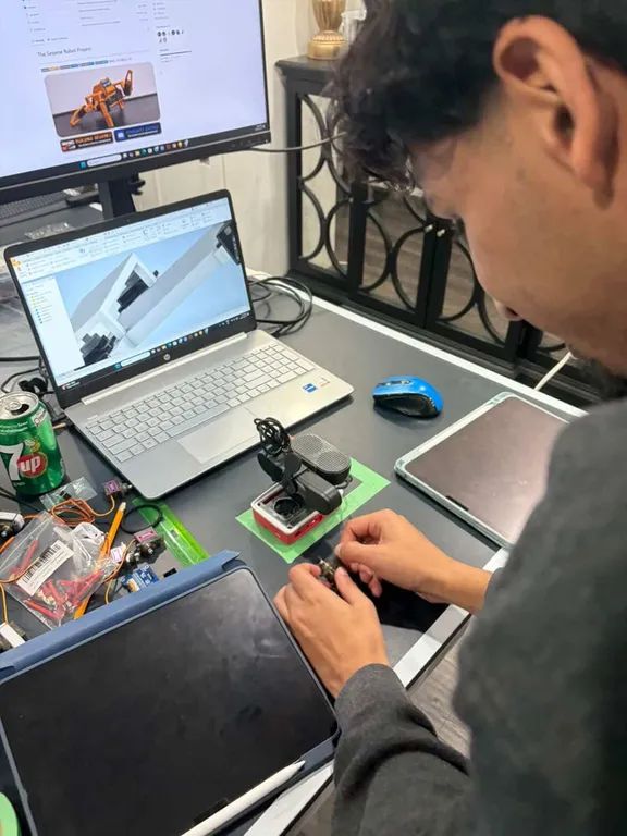Working on a small servo by hand at the desk, with the CAD model open on the laptop beside it.