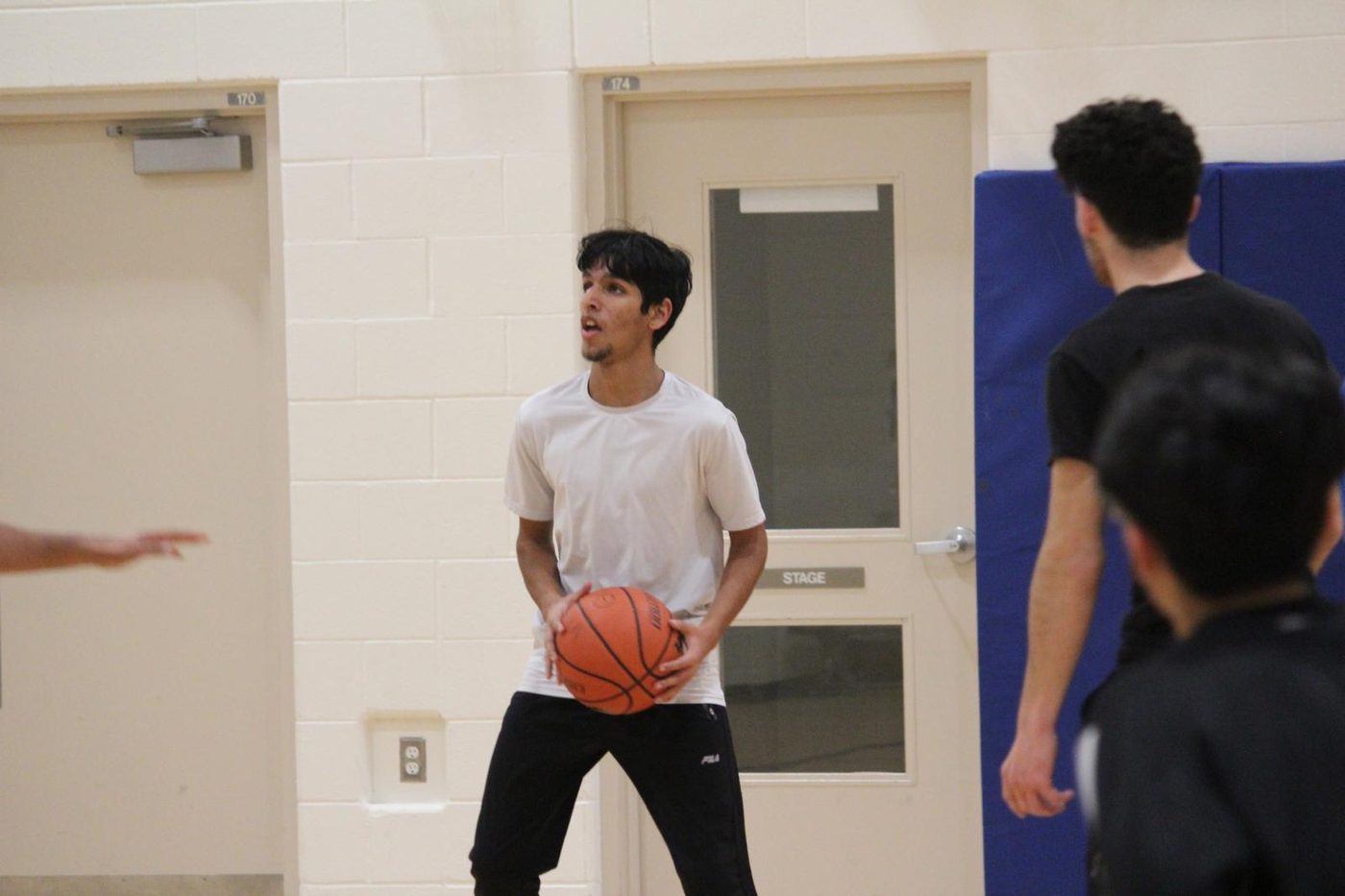 Holding a basketball at the top of the key in a gym while two other players close in.