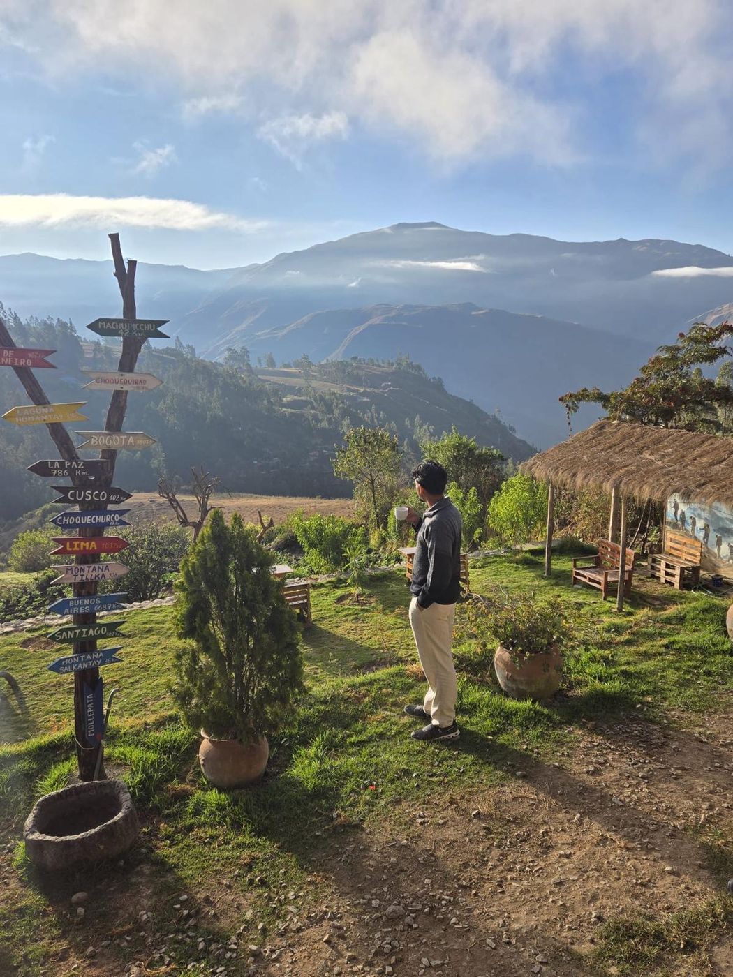A post of painted wooden direction arrows on a ridge, one reading Cusco, with mist over the mountains behind.